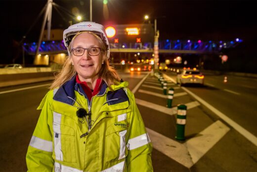 Personne en chasuble et casque sur une route nocturne, pont éclairé et voitures derrière : engagement sécurité VINCI.