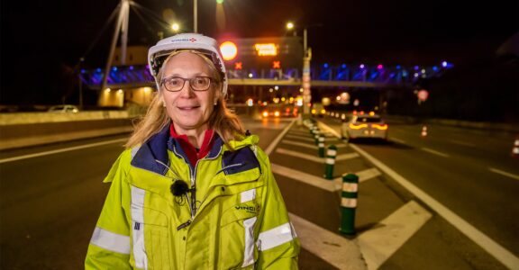 Personne en chasuble et casque sur une route nocturne, pont éclairé et voitures derrière : engagement sécurité VINCI.